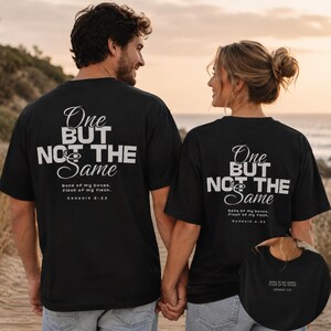 Puede incluir: Dos personas con camisetas negras con el texto "One BUT NOT THE Same" en letras blancas. Las camisetas también incluyen el texto "Bone of my bones. Flesh of my flesh. Genesis 2:23". La pareja se toma de la mano.