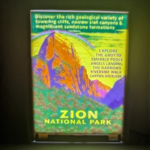 Peut inclure: Un panneau rétroéclairé avec une illustration colorée du parc national de Zion. L'image présente des falaises et des canyons imposants, avec le texte "Zion National Park". Du texte supplémentaire met en évidence les caractéristiques géologiques et les attractions.