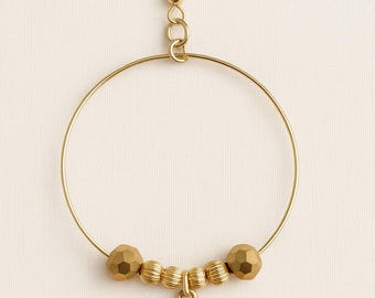 May include: Gold-toned hoop earring with a decorative charm. The earring features a large circular hoop, faceted beads, and a cross-shaped pendant. The earring's hook and connecting elements are also gold-toned, creating a cohesive and elegant design.