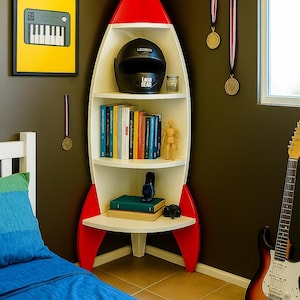 Peut inclure: Une étagère en forme de fusée blanche et rouge avec un casque noir, des livres et des objets décoratifs. Une œuvre d'art encadrée d'un clavier est accrochée au mur. Une guitare est appuyée contre le mur. Des médailles sont suspendues au plafond.