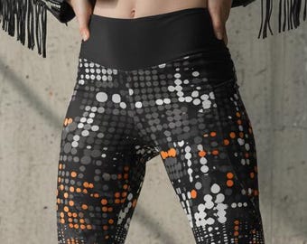May include: High-waisted leggings featuring a black base with a repeating pattern of white, gray, and orange circular dots of varying sizes. The leggings have a wide, solid black waistband and extend down to the ankles, paired with black boots.