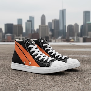 May include: Pair of high-top sneakers with a black base and a bold orange diagonal stripe design. The sneakers have white laces, a white toe cap, and a white sole. The background features a cityscape with tall buildings.
