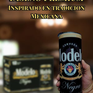 May include: A black Modelo Negra beer can with gold accents is held in a hand. The can features the Modelo logo, the words "Negra" and "Cerveza", and the text "BREWED IN MEXICO". The background includes a blurred six-pack of Modelo Negra.