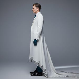 May include: A long, white coat with a flowing train and ornate black embroidery along the hem. The coat features a tailored fit, a notched lapel, and buttoned cuffs. The person is wearing a teal tie and gloves, and black dress shoes.