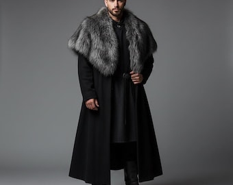 May include: A full-length black coat with a gray fur collar. The coat has a belt at the waist and is worn with black boots. The person is standing in front of a gray background. The coat is a medieval style.