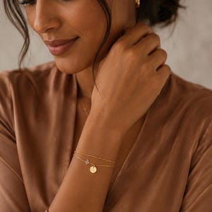 Peut inclure: Un bracelet double rang en or composé d'une fine chaîne perlée et d'une seconde chaîne ornée d'une petite étoile scintillante à quatre branches ainsi que d'un pendentif circulaire gravé de la lettre A.