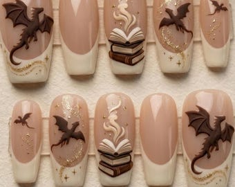 May include: A set of ten press-on nails featuring a nude base with cream-colored French tips. Designs include raised 3D brown dragons, stacks of books with swirling smoke, and gold glitter accents in the shape of stars and flowing trails.