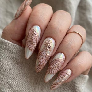 May include: Almond-shaped nails featuring a pearlescent white base with raised, metallic rose gold relief designs. The artwork depicts intricate bird wings and a stylized peacock motif across the nails, creating a textured, three-dimensional effect.