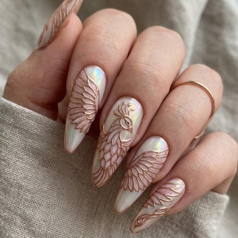 May include: Almond-shaped nails featuring a pearlescent white base with raised, metallic rose gold relief designs. The artwork depicts intricate bird wings and a stylized peacock motif across the nails, creating a textured, three-dimensional effect.