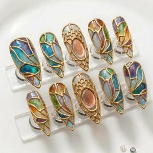 May include: A set of ten long, almond-shaped nail art designs. Each nail features a stained-glass effect with gold-colored metal outlines and a variety of colors, including blue, green, orange, and purple.
