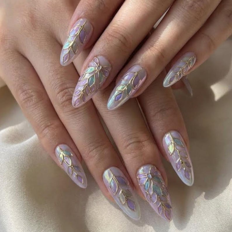 May include: Long, almond-shaped nails with a pearlescent finish. Each nail features a gold outline design with iridescent leaf-like shapes in shades of purple, green, and blue. The nails are well-manicured and reflect light.
