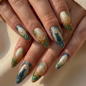 May include: Almond-shaped nail art with a gold trim and intricate designs. The nails feature a cat silhouette, gold stars, and green leaf accents. The color palette includes teal, gold, and iridescent white.