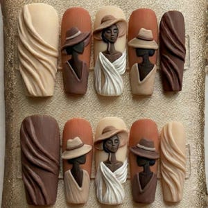 May include: A set of ten artificial nails with a neutral color palette. The nails feature 3D art of women wearing hats and draped fabric. Some nails have a textured, swirled design in shades of brown and beige.