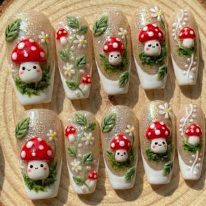 May include: A set of ten artificial nails with a whimsical mushroom theme. Each nail features a beige glitter base, white tips, and 3D mushroom and floral designs in red, white, and green. The mushrooms have smiling faces.