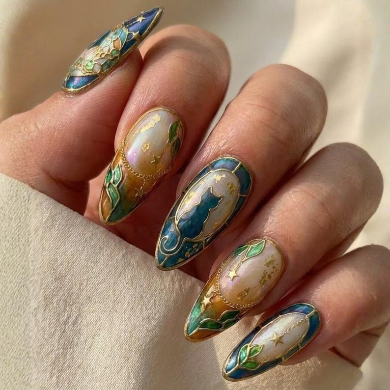 May include: Detailed nail art featuring an oval shape with a cat silhouette, stars, and floral designs. The nails have a gold trim and a pearlescent base with blue, green, and gold accents. The design is intricate and elegant.