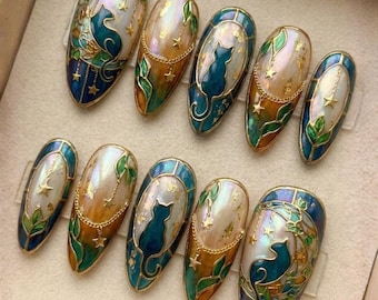 May include: A set of ten oval-shaped, painted fingernails. Each nail features a teal cat silhouette, gold stars, and gold chain accents. The nails have a pearlescent base with teal, gold, and green details, and a gold border.