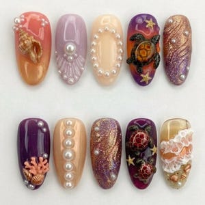 May include: A set of ten artificial nails with various designs. The nails feature a range of colors, including orange, purple, and gold, and are adorned with pearls, seashells, and sea turtles. Some nails have glitter accents.
