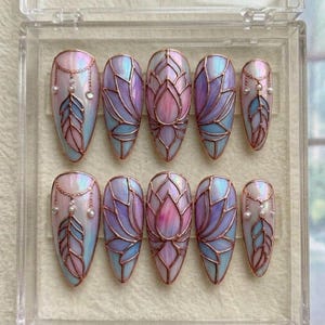 May include: A set of ten artificial nails with a stained glass design. The nails feature a copper-colored outline with pastel pink, blue, and purple hues. Some nails have a feather and pearl accents.
