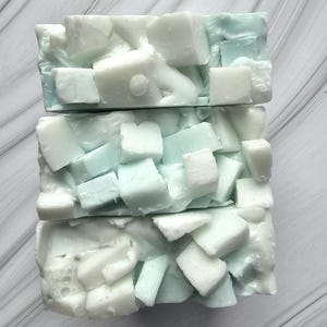 May include: Three bars of handmade soap, each with a unique design. The soap features a base colour of light blue, with white chunks embedded throughout. The bars are stacked on top of each other, creating a layered effect.