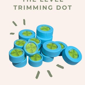May include: A pile of blue level trimming dots, each with a green and yellow bubble level. The text "THE LEVEL TRIMMING DOT" is at the top. The Pearl & Fern Co. logo is at the bottom of the image.