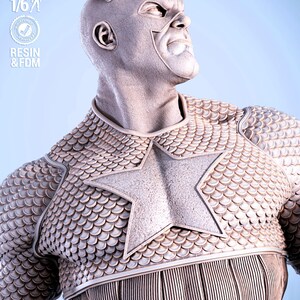 May include: A gray, detailed statue of a superhero figure, featuring a star emblem on the chest and scale-like armor. The figure is wearing a mask and has a determined expression. The image includes text indicating scale and material.