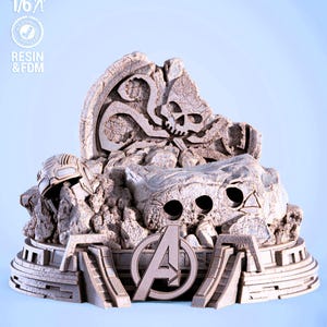 May include: A detailed, light-colored resin sculpture featuring the Avengers logo, a skull, and a helmet. The base has a tiered design with the text "RESIN & FDM" and "SCALE 1/6". The sculpture has a weathered, stone-like appearance.