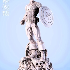 May include: A detailed statue of Captain America in a dynamic pose, holding his shield. The figure is in a light color, standing on a rocky base with the Avengers logo. The statue is labeled "SCALE 1/6" and "RESIN & FDM".