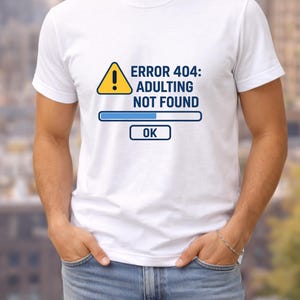 May include: White t-shirt featuring the text "ERROR 404: ADULTING NOT FOUND" in black, with a yellow warning sign and a blue loading bar graphic. The word "OK" is in a blue box below the loading bar.