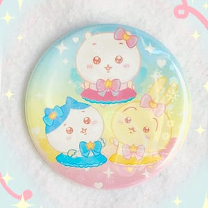 May include: A round button featuring three cartoon characters: a bear, a cat, and a rabbit. Each character has a bow and star-shaped accents. The button has a gradient background of blue, yellow, and pink.