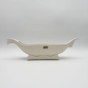 May include: White ceramic boat-shaped planter with a raised base and a "Pleasant" label on the side.