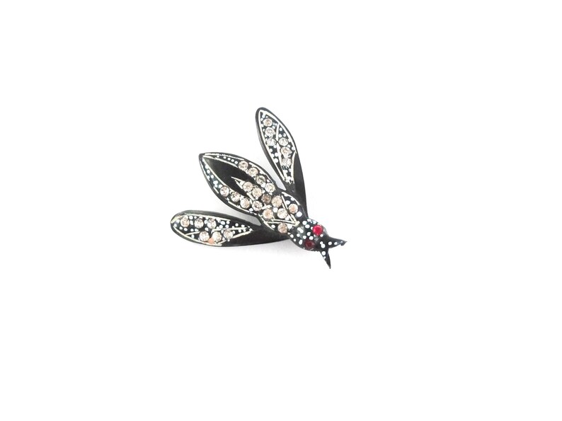 May include: A black and silver insect brooch with three wings. The wings are adorned with clear and red rhinestones. The brooch is set against a white background.