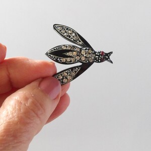 May include: A vintage insect brooch with a black enamel body and wings, adorned with sparkling clear rhinestones. The insect's head features a small red accent, adding a pop of color to the elegant design. A classic piece of jewelry.