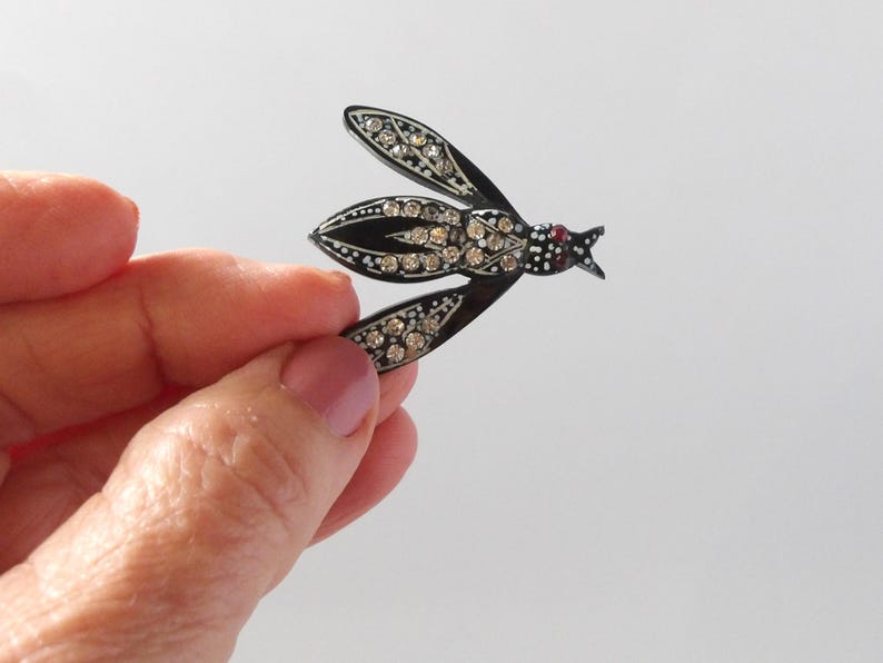 May include: A vintage insect brooch with a black enamel body and wings, adorned with sparkling clear rhinestones. The insect's head features a small red accent, adding a pop of color to the elegant design. A classic piece of jewelry.