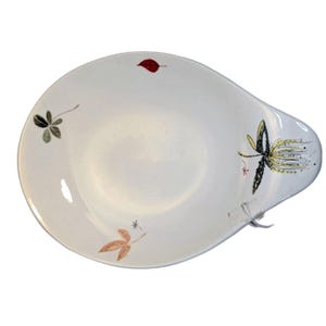 May include: White ceramic serving dish with a unique handle. The dish is decorated with colorful leaf and floral designs in red, black, and yellow. A stylish piece for serving appetizers or small dishes.