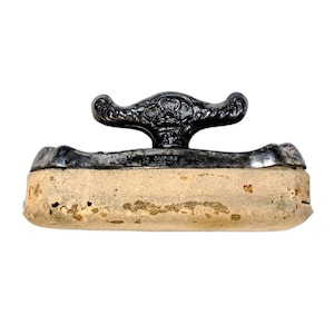 May include: An antique Empire clothes iron with a decorative handle. The handle is dark metal with ornate detailing. The iron's base is a light tan color, showing signs of age and use. The word "EMPIRE" is visible on the iron.