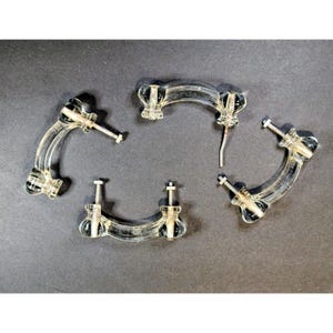 May include: Four clear acrylic drawer pulls with a curved, arch-shaped design. Each handle features two metal mounting posts with threaded ends for installation. The hardware is transparent, showcasing a smooth, glossy finish throughout the pieces.