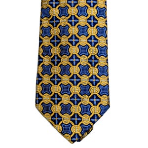 May include: A patterned tie with a repeating design of gold interlocking circles and squares on a navy blue background. The tie has a classic shape and is made of a smooth material, possibly silk.
