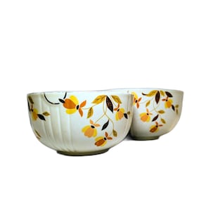 May include: Two off-white ceramic bowls with a floral pattern in yellow, orange, and brown. The bowls have a ribbed texture and a curved shape. The floral design includes stylized flowers and leaves.