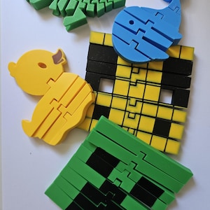 May include: A selection of colourful foam puzzles shaped like a green dinosaur skeleton, a blue whale, a yellow duck, a green pixelated face, and a yellow and black grid. These educational toys are designed for children.