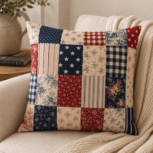 May include: A square throw pillow featuring a patchwork design with various fabric patterns in red, white, and blue. The squares include motifs such as white stars on a navy background, red and white gingham, floral prints, and vertical stripes.