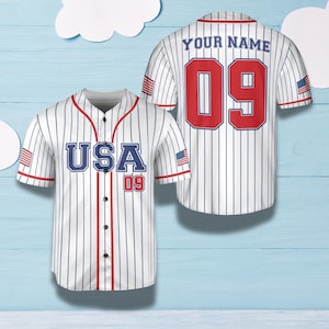 May include: White baseball jersey with vertical blue stripes, displaying "USA" and the number "09" in red and blue. The jersey has red trim and small American flags on the sleeves. The back of the jersey shows "YOUR NAME" and the number "09".