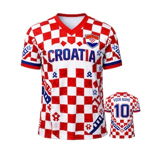 May include: A red and white checkered Croatia soccer jersey with the word "CROATIA" across the chest. The jersey has a V-neck and a Croatian coat of arms on the upper right chest. A smaller jersey is shown on the right.