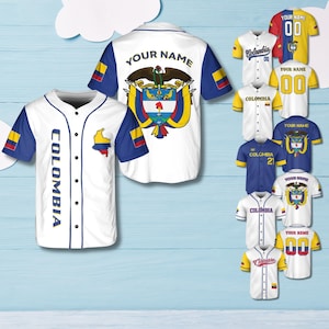 Peut inclure: Maillots de baseball blancs avec des détails bleus et jaunes, affichant "COLOMBIA" et un graphique de carte. D'autres maillots affichent "YOUR NAME" et le numéro "00", ainsi que les armoiries colombiennes.
