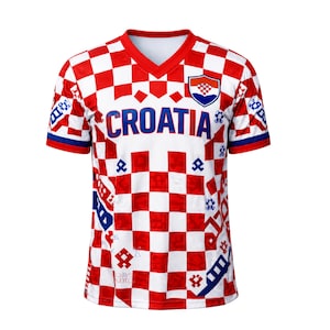 May include: A Croatia soccer jersey with a red and white checkered pattern. The jersey has a V-neck collar and the word "CROATIA" in blue across the chest. The Croatian coat of arms is on the upper right chest.