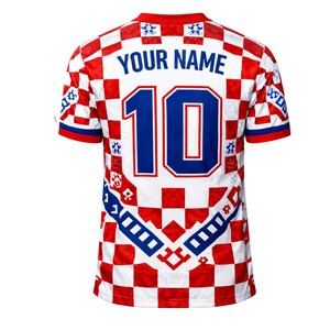 May include: A white and red checkered soccer jersey with blue accents. The jersey features the number 10 in blue, with the text "YOUR NAME" above it. The sleeves and collar are red and blue.