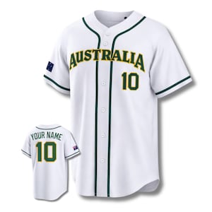 Op de afbeelding: Wit honkbalshirt met groene en gouden accenten. Het woord "AUSTRALIA" staat in een boog over de borst, met het nummer "10" eronder. Een kleiner shirt toont "YOUR NAME" en het nummer "10" op de rug.