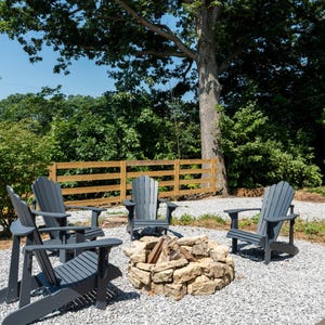 May include: An outdoor seating area featuring a fire pit and grey Adirondack chairs. The chairs are arranged around a stone fire pit. The area is surrounded by trees and a wooden fence, creating a relaxing outdoor space.