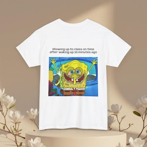 Op de afbeelding: Een wit T-shirt met korte mouwen en een afbeelding van een vermoeid uitziende Spongebob Squarepants met rode ogen en een brede grijns. Boven de afbeelding staat de zwarte tekst: Showing up to class on time after waking up 10 minutes ago.