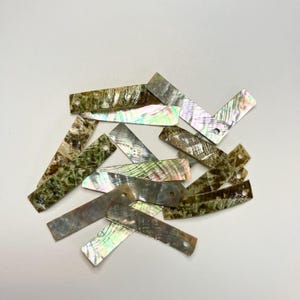 May include: A collection of rectangular, iridescent abalone shell pieces. The shells have a natural, textured appearance with shades of green, brown, and silver. Each piece has a small hole, suggesting they are intended for crafting or jewelry making.