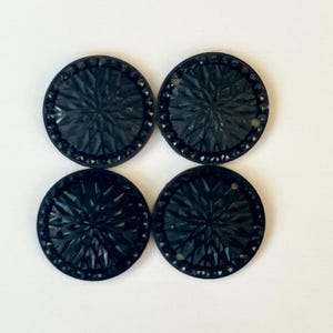 May include: Four black, round buttons with a detailed, geometric design. Each button has a central starburst pattern and a beaded edge. The buttons are arranged in a square formation against a white background.